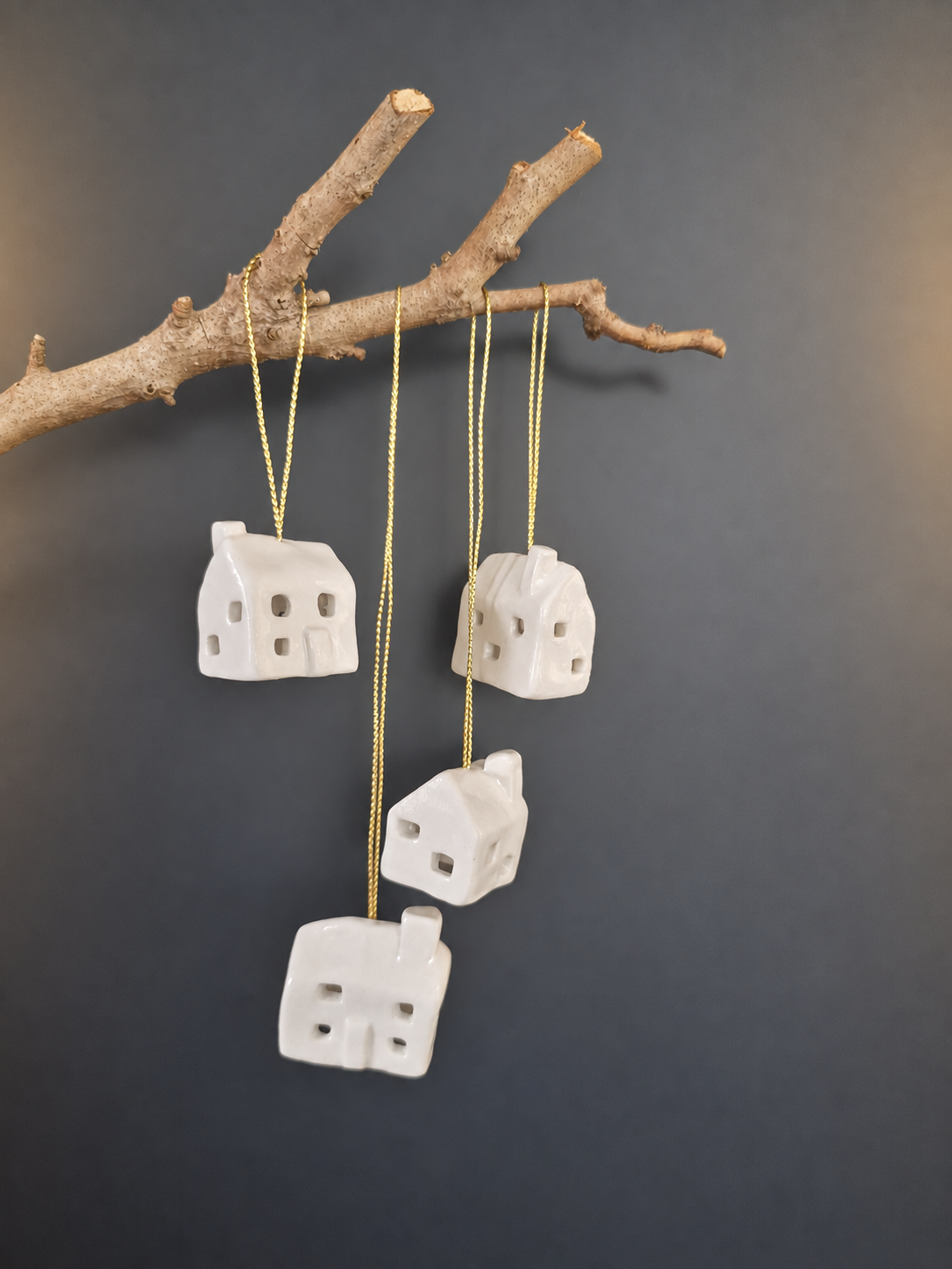 Four white ceramic house ornaments hanging from branch with gold string