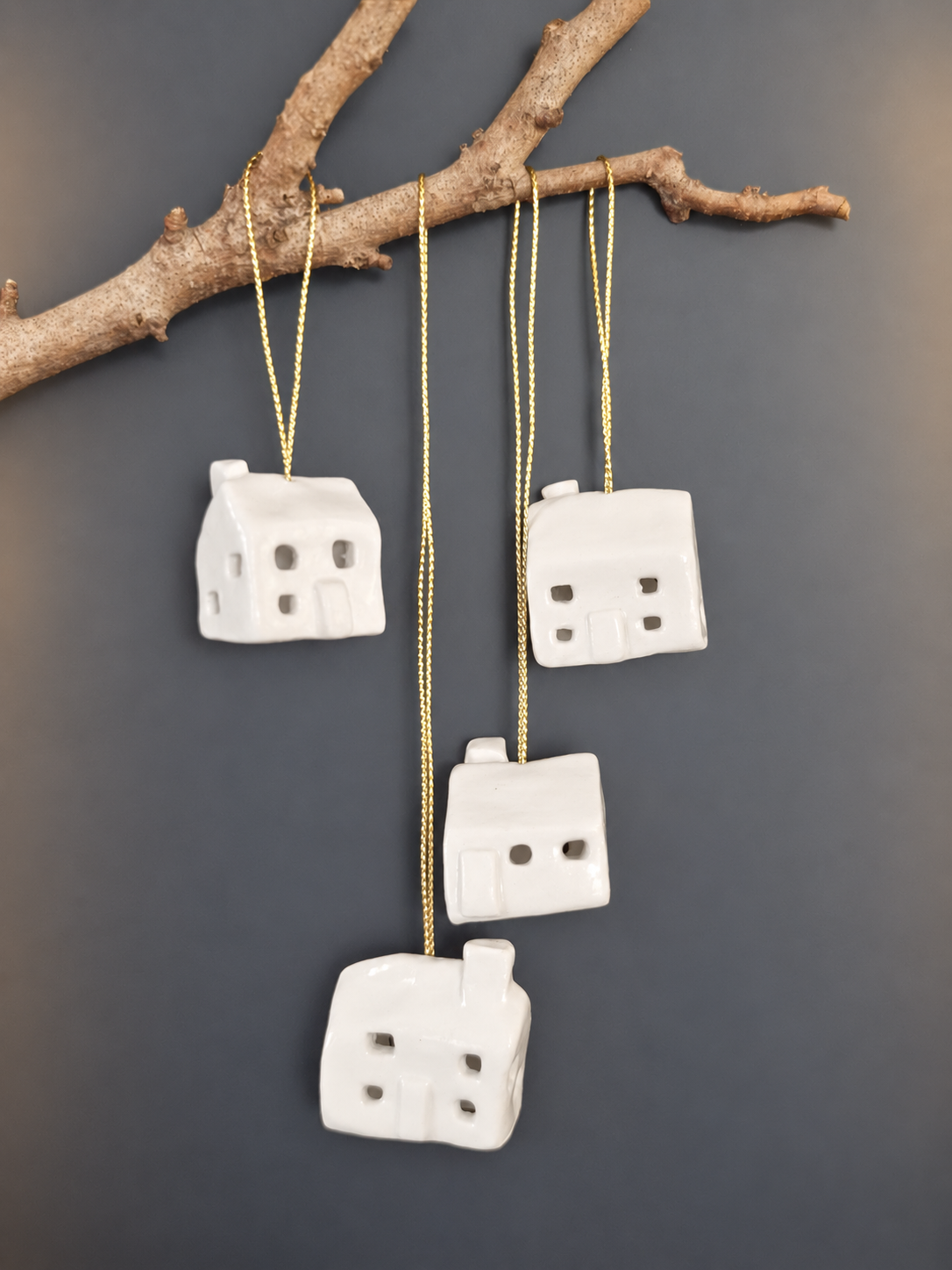 Four white ceramic house ornaments hanging from branch alternative view