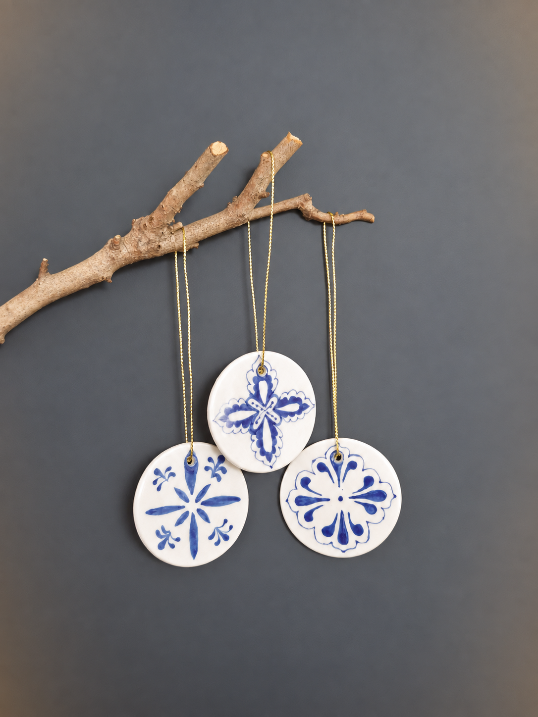 Three blue and white hand-painted ceramic disc ornaments hanging from branch with gold string